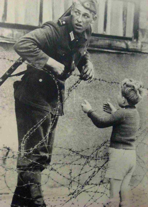 24. "Buradan kimse geçmeyecek" emrine karşın bir Batı Alman askeri ailesine kavuşması için küçük çocuğun tel örgüleri aşmasına yardım ediyor. (Berlin, 1961)