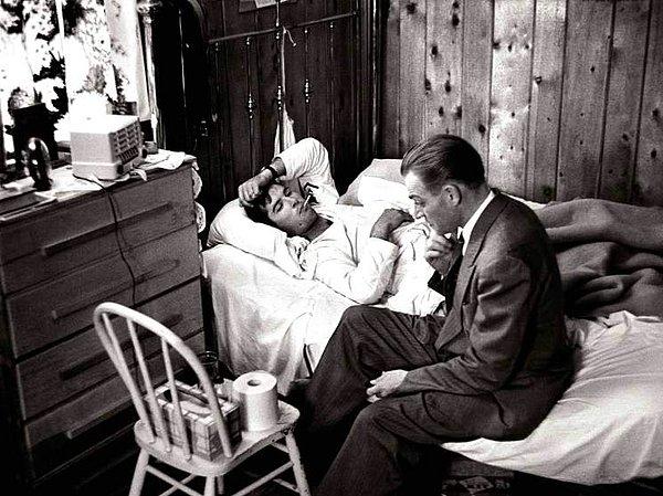 3. Ceraini gripli hastasının yatağının kenarına oturuyor.