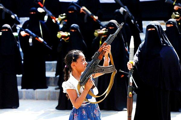 12. Yemen'de bir geçit töreni sırasında bir kız, Houthi sadıklarından olan kadınların önünde silah tutuyor.