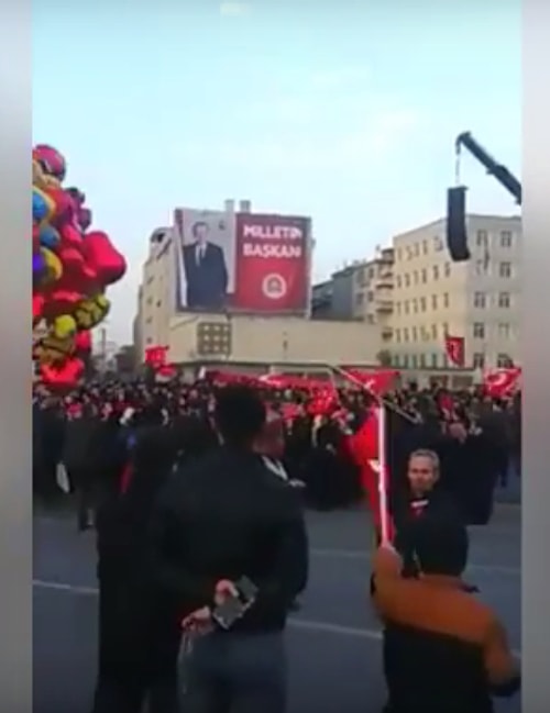 Bazı vatandaşların dans ettiği görüntülere ilişkin videonun 10. saniyesinde, arka tarafta bir binada yer alan “Milletin Başkanı” yazılı afiş, mitingin olduğu gün çekilen farklı bir videoda da görülüyor.
