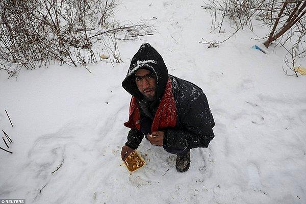 Bu göçmen yemek almayı başarabilmiş ve zor hava şartlarında yemeye çalışıyor.
