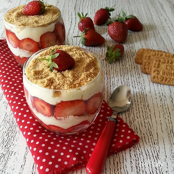 Поверх крема снова кладем по одной столовой ложке печенья и украшаем клубникой.