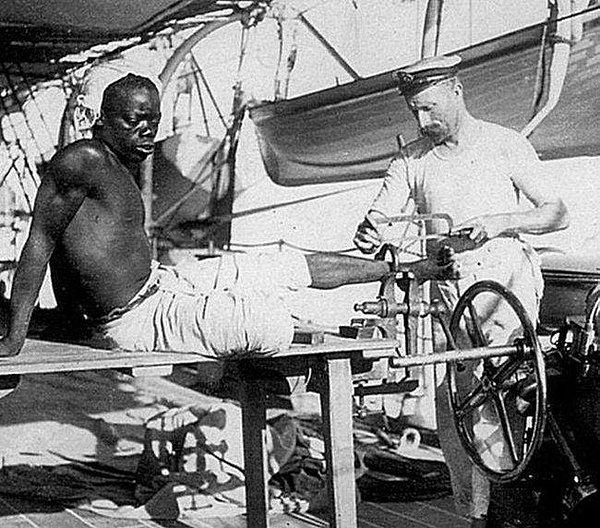 18. İngiliz Kraliyet Donanması'ndan bir denizci, kurtarılan kölelerden birinin ayağına takılmış demiri testereyle keserken, 1907.