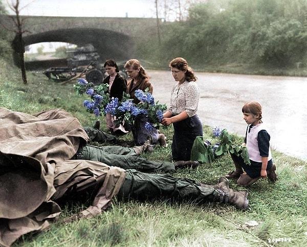 2. ABD ordusu tarafından çalışma kampından kurtarılmalarının ardından üç Rus kadın ve küçük bir kız, 4 ölü ABD askerinin ayak ucuna çiçekler bırakırken, Hilden, Almanya, 18 Nisan 1945.