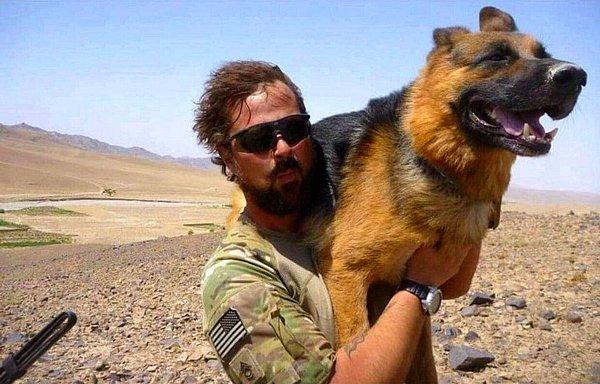 41. Hava çok sıcak olduğu için patileri yere bastığında yanan rehber köpeği omzunda taşıyan bir asker.