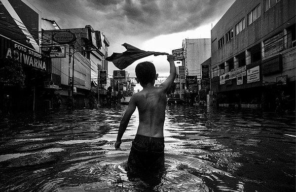 Küçük bir çocuk, sokakları dolduran sel sularında oynuyor, Jakarta.