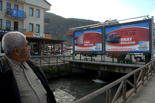 Saatcı'dan Halkın Takdirini Kazanan 10 Hareket 6 Fethiye’de gerçekleştirmek istediği kruvaziyer liman, körfezin temizliği ve yat çekek yeri gibi projelerin başlamasına onay vermeyip bekleten Ankara’daki dönemin bakanlarını, şehir billboardlarıyla halka şikâyet etti.