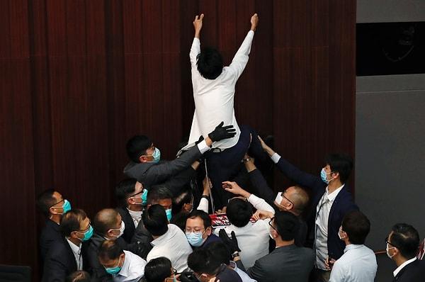 Milletvekili Eddie Chu Hoi-dick ise komite başkanlığı koltuğuna ulaşmak için duvara tırmanmaya çalışırken 4 güvenlik görevlisi tarafından salon dışına çıkarıldı.