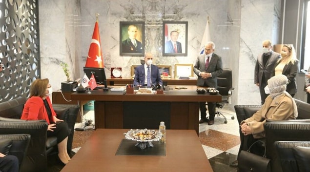 Fotoğrafta Kurtulmuş’un, rektörün makam koltuğunda, rektör Özaydın’ın da aralarında bulunduğu bazı kişilerin ise ayakta, ellerini önde kenetlemiş şekilde durduğu görülüyor.