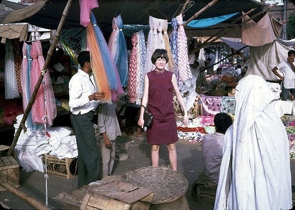 12. Kadınların kara çarşaflarla kısıtlanmadığı ve kendi başına rahatça sokaklarda gezebildiği bu yıllarda, giyim tercihleri de oldukça renkliydi. Fotoğrafta da pazardan eşarp alan bir kadın görülüyor.