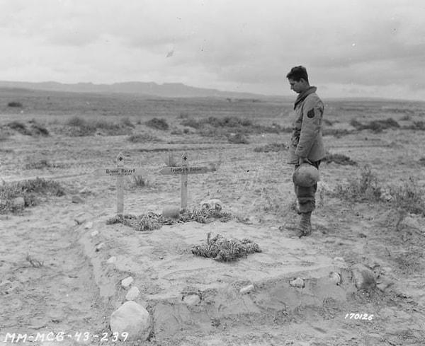 7. ABD Ordusundan Çavuş. T. B. Haber, Tunus'taki Kasserine Geçidi Muharebesi sırasında öldürülen iki Alman askerinin mezarlarının yanında duruyorken. (26 Şubat 1943)